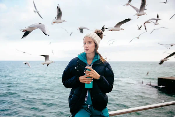 Zamyšlná dívka držící termosku u moře s racky — Stock fotografie