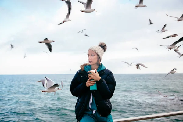 Tankeväckande kvinna med termos nära havet med måsar Stockfoto