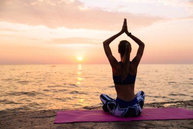 Spor kadını yoga yapıyor, iskelede oturuyor, deniz kenarında.