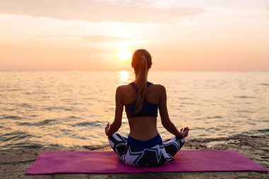 İnce kız yoga yapıyor, iskelede oturuyor, deniz kenarında.