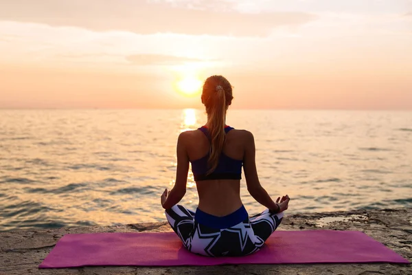 Slim dziewczyna praktykuje jogę, siedzi na molo, nad morzem Zdjęcie Stockowe