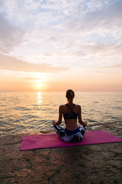 Ung kvinna som utövar yoga, sitter på piren, vid havet Stockbild