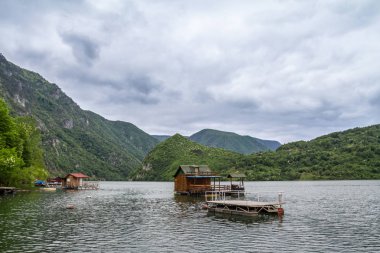 Fishemen floating houses on Perucac lake, on the Drina river, in Western Serbia, surrounded by a valley and narrow canyon and a forest made of pine trees during a cloudy afternoon clipart