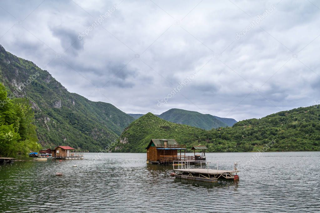 Fishemen floating houses on Perucac lake, on the Drina river, in Western Serbia, surrounded by a valley and narrow canyon and a forest made of pine trees during a cloudy afternoon