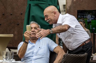 Belgrade, Sırbistan - 14 Haziran 2015: iki eski sernior beyaz adam bir Apple Iphone smartphone vasıl arıyorsunuz bir kafede otururken, bir ikinci nasıl kullanılacağını açıklayan