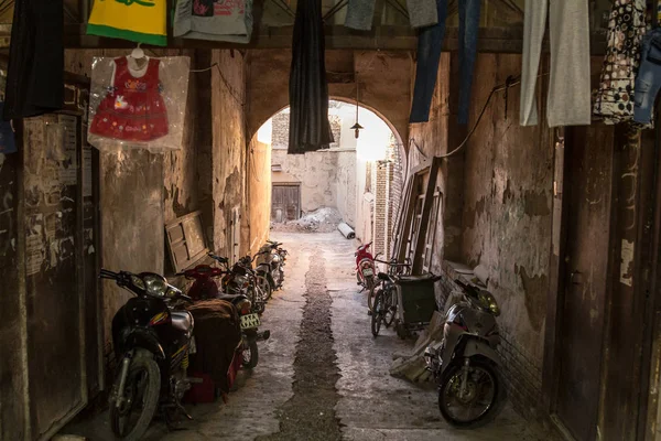 YAZD, IRAN - AUGUST 17, 2018:  Motorcycyles, scooters, motorbikes and bicycles parked in a typical street of the old town of Yazd,  with its typical clay walls & buildings. Yazd is the main city of Central Iran