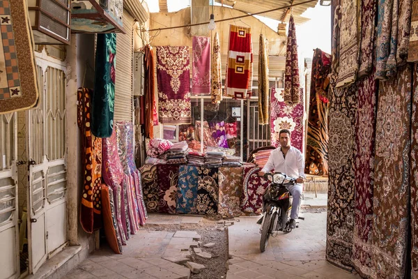 Yazd, Iran - 18 Ağustos 2015: halı ve kilim Yazd Khan'ın Bazaarı satış mağazaları ile çevrili bir motosiklet sürüş adam. Yazd Orta İran'ın ana kentlerinden biridir