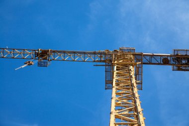 Güneşli bir öğleden sonra, mavi bir gökyüzünün altında, aşağıdan alınan bir inşaat alanında toplanan bir binanın önündeki sarı metal vinç.