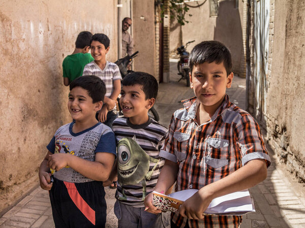 YAZD, IRAN - AUGUST 18, 2015: Group of iranian Pupils, boys, primary and secondary school students, standing and playing , one holding a study notebook, in Yazd, in Central Iran