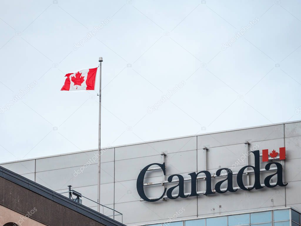 OTTAWA, CANADA - NOVEMBER 10, 2018: Canada Wordmark, the official logo of the Canadian government, on an administrative building next to a Canadian flag waiving