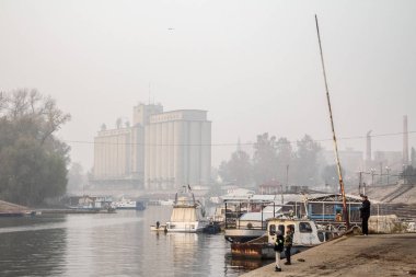 Pancevo, Sırbistan - Kasım 2015: Çocuk Pancevo sahildeki Tamiş nehrinde sisli bir öğleden sonra boyunca balık tutma. İkonik silolar arka planda görülebilir.