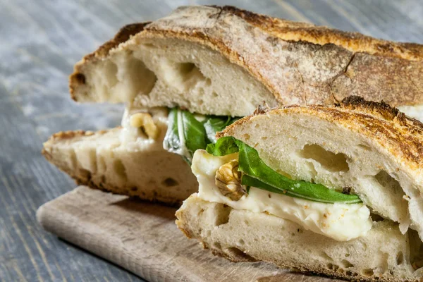 Close up Brie sanwdich in a French baguette, made of Brie de Meaux Cheese with some slices of rucola salad and walnuts on display on a rustic wooden table. This sandwich, in France, is called sandwich au brie