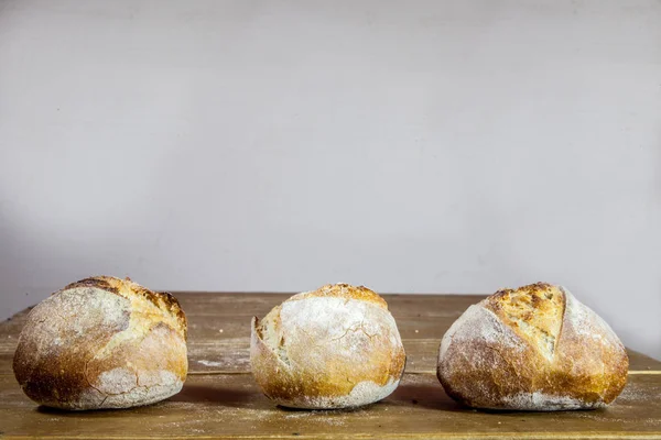 Three small loafs of French bread on display on a rustic wooden table, baguette style. They are called in French petits pains, made of yeast called levain