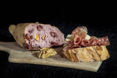 Fransız ekşi hamur Somun, ayrıca Pain de campagne denir, önünde kurutulmuş sosis (saucisson, bir Fransız tedavi et) ile ekmek bir dilim ile siyah bir arka plan üzerinde et ve ceviz ile doldurulmuş