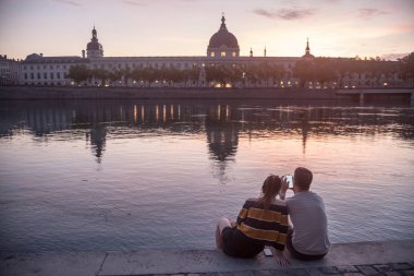 Lyon, Fransa-Temmuz 18, 2019: çift, severler, Rhone Nehri kıyısında bir smarthone bakarak, Quais de Rhone üzerinde, Hotel Dieu, şehrin ana anıtlarından biri karşı karşıya