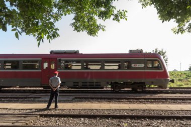 Alibunar, Sırbistan - 30 Haziran 2019: Alibunar tren istasyonundan geçen bölgesel Dmu treni, şebekenin yönetiminden sorumlu bir demiryolu işçisi olan istasyon şefi tarafından izleniyor