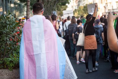 Eşcinsel bir gurur sırasında arkadan görülen transseksüel bayrağa sarılmış bir adam. Bu bayrak Lgbtq ve transseksüel insanların ve toplumun sembollerinden biridir.