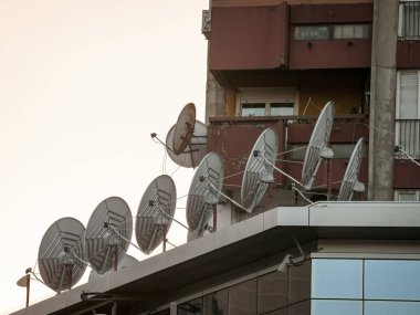 Günbatımında bir iş binasının tepesinde uydu çanakları ve antenler sergileniyor. Bunlar iletişim ve bilgi iletimi için kullanılır..