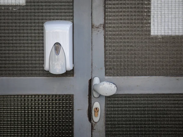 Hand sanitizer dispenser mounted on the wall of entrance door with a lock and knob, in public place, a residential building, distributing hydroalcoholic gel during the coronavirus covid 19 crisis