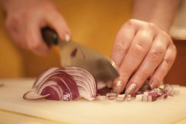 Kadınların elleri kırmızı soğanları bıçakla kesiyor, beyaz bir kalas üzerinde, hız bulanıklığı ve soğanlara odaklanma ile, diğer adıyla allium sepa