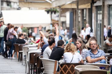 BELGRAD, SERBIA - 3 Eylül 2018: Orta yaşlı bir adam kameraya bakıyor, Belgrad şehir merkezindeki bir kafe ve restoranın terasında oturuyor ve arka planda eğlenen bir kalabalık var.
