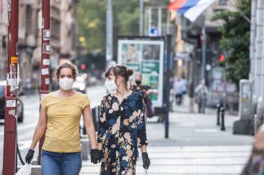 BELGRAD, SERBIA - 6 Haziran 2020: Genç insanlar, iki genç bayan arkadaş, Coronavirus Covid 19 krizinde yüz maskesi koruyucu ekipman ve latext eldiven takarak yürüyorlar
