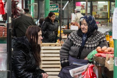 BELGRAD, SERBIA - 31 Ocak 2016: Geleneksel giysi ve meyve ve sebze satan yaşlı kadın, Zeleni Venac Pijaca Green pazarında genç bir kadınla tartışıyor. Sırp tarımının bir simgesi.