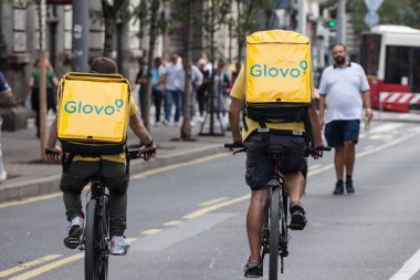 BELGRAD, SERBIA - 28 Eylül 2019: Belgrad 'da bisikletleriyle gezen iki teslimatçının çantasındaki Glovo logosu. Glovo, Avrupa 'da yayılmış bir İspanyol Gıda dağıtım uygulaması.