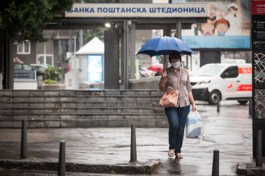 BELGRAD, SERBIA - 17 Temmuz 2020: Coronavirus covid 19 sağlık krizi sırasında, Belgrad caddesinde şemsiyesi altında yürüyen, solunum maskesi takan yaşlı kadın