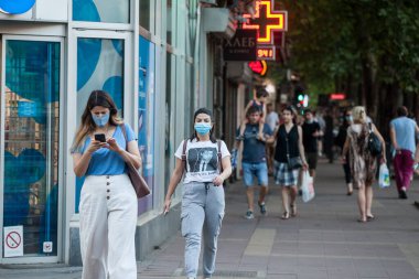 BELGRAD, SERBIA - 28 Temmuz 2020: Coronavirus covid 19 sağlık krizi sırasında Belgrad caddesinde akıllı telefonlarındaki uygulamaları kontrol eden solunum maskesi takan iki genç kadın