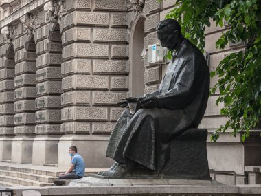 BELGRAD, SERBIA - 23 Temmuz 2020: Genç bir adam, bilim adamı Nikola Tesla 'nın Coronavirus Covid 19 krizinde yüz maskesi takan bir heykelinin önünde oturuyor