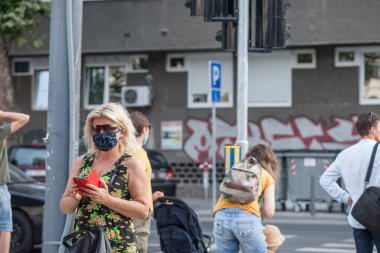 BELGRAD, SERBIA - 4 AĞUSTOS 2020: Solunum maskesi takan yaşlı bir kadın, koronavirüs kovid 19 sağlık krizi sırasında kuyrukta bekleyen bir akıllı telefondan uygulamalarını kontrol ediyor