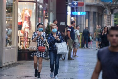 BELGRAD, SERBIA - 5 Ağustos 2020: Genç insanlar, iki genç bayan arkadaş, Coronavirus Covid 19 krizinde yüz maskesi koruyucu ekipman takarak el dezenfektanı ile yürüyorlar