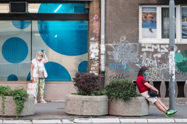 BELGRAD, SERBIA - 21 AĞUSTOS 2020: İki kişi, genç bir adam ve yaşlı bir kadın, Coronavirus Covid 19 krizinde maske takmış otobüslerini Belgrad 'da bekliyorlar.