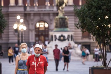 BELGRAD, SERBIA - 26 Ağustos 2020: Yaşlı bir adam çenesinin altına solunum maskesi takarken genç bir kız Coronavirus covid 19 sağlık krizi sırasında doğru bir şekilde maske takıyor