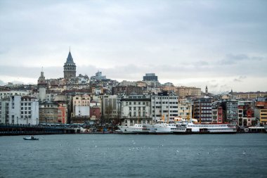 Karaköy ve Beyoğlu 'ndaki tepesinde yer alan Galata Kulesi bulutlu bir kış öğleden sonra alınırken, İstanbul, Türkiye' de deniz, feribot ve kargo gemileri ön planda görülebiliyor.