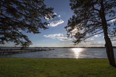 Sırbistan 'ın Subotica kentindeki Paliç Gölü' nde, sonbahar günbatımında arka planda çam ağaçları ve yeşil bir çimen bulunuyor. Palicko Jezero olarak da bilinen festival, Voyvodina 'nın başlıca etkinliklerinden biri.