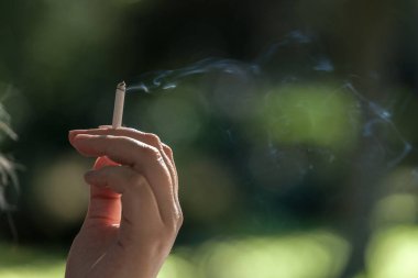 Closeup on female hands of a woman with fingers holding a cigarette butt with a filter lit, smoking with its toxic fumes.