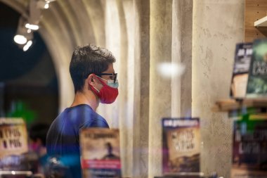 BELGRAD, SERBIA - SEPTEMBER 15, 2020: Müşteri, genç adam, Coronavirus covid 19 sağlık krizi sırasında Belgrad 'da bir yerine iki solunum maskesi takmış bir kitapçıda duruyor