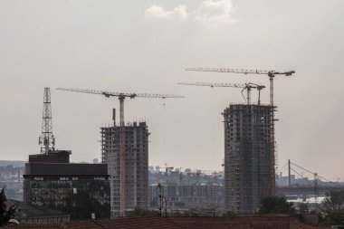 Bir emlak geliştirme alanında inşaat iskeleleri, beton ve beton cepheleri ve vinçleri olan gökdelen kulelerinden oluşan bir bina kompleksinin panoraması.