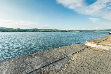 Tuna Nehri, Sırbistan 'ın Veliko Gradiste kentinde bulunan bir rıhtımdan Demir Kapılar, Cerdap Vadisi ve Romanya kıyılarına doğru geniş bir görüş alanına sahip. Mavi su, uzak tepeler ve açık gökyüzü sakin bir manzara yaratır..