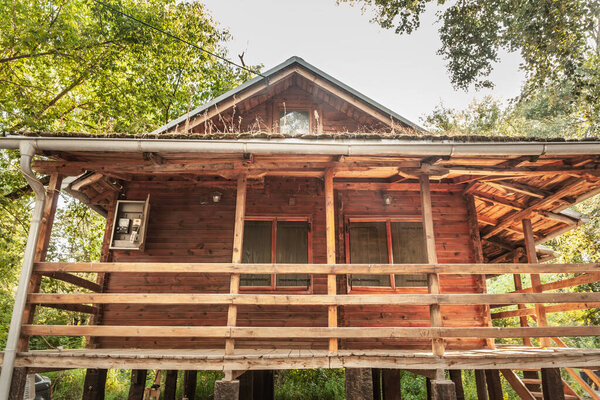 Exterior of a wooden weekend house, known locally as a vikendica, with balcony and gable roof in a wooded setting in Serbia. Rustic construction and elevated porch suggest a simple countryside retreat