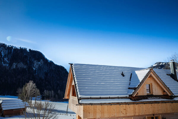 Деревянное альпийское шале в Словении с заснеженной крышей. Изображение подчеркивает изоляцию крыши и конструкцию холодного климата, с облицовкой из древесины, фронтальным окном и чистым зимним горным освещением