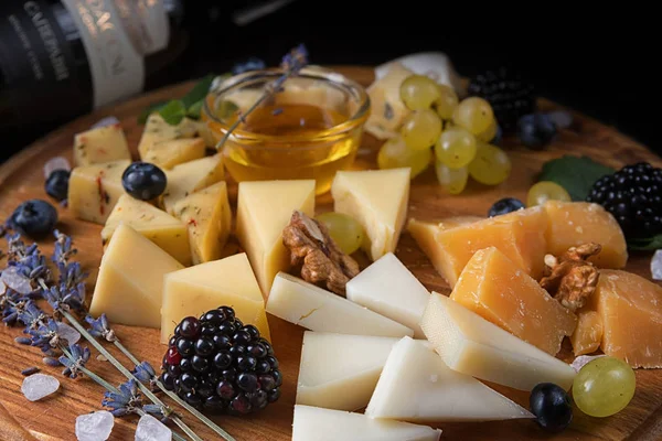 Cheese platter on a wooden board with fruits and herbs