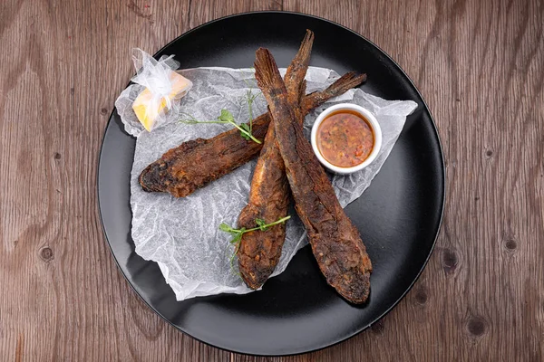 Pescado frito en un plato negro, Gobies —  Fotos de Stock