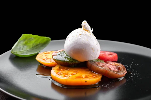 Buratta mozzarella with pesto sauce and tomatoes on a black plat — Stock Photo, Image