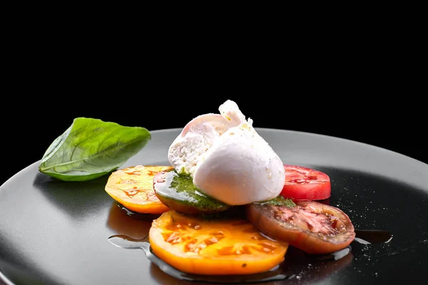 Buratta mozzarella with pesto sauce and tomatoes on a black plat — Stock Photo, Image