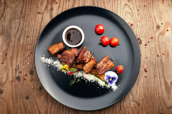 Fried ribs on a black plate with sauce and tomatoes — Stock Photo, Image