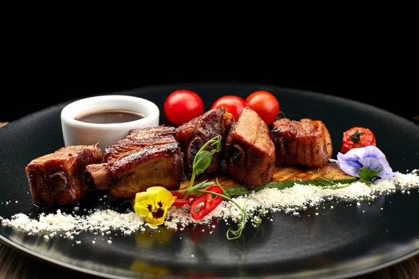 Côtes frites sur une assiette noire avec sauce et tomates — Photo