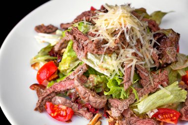 Beyaz tabakta et ve peynirli sıcak salata.